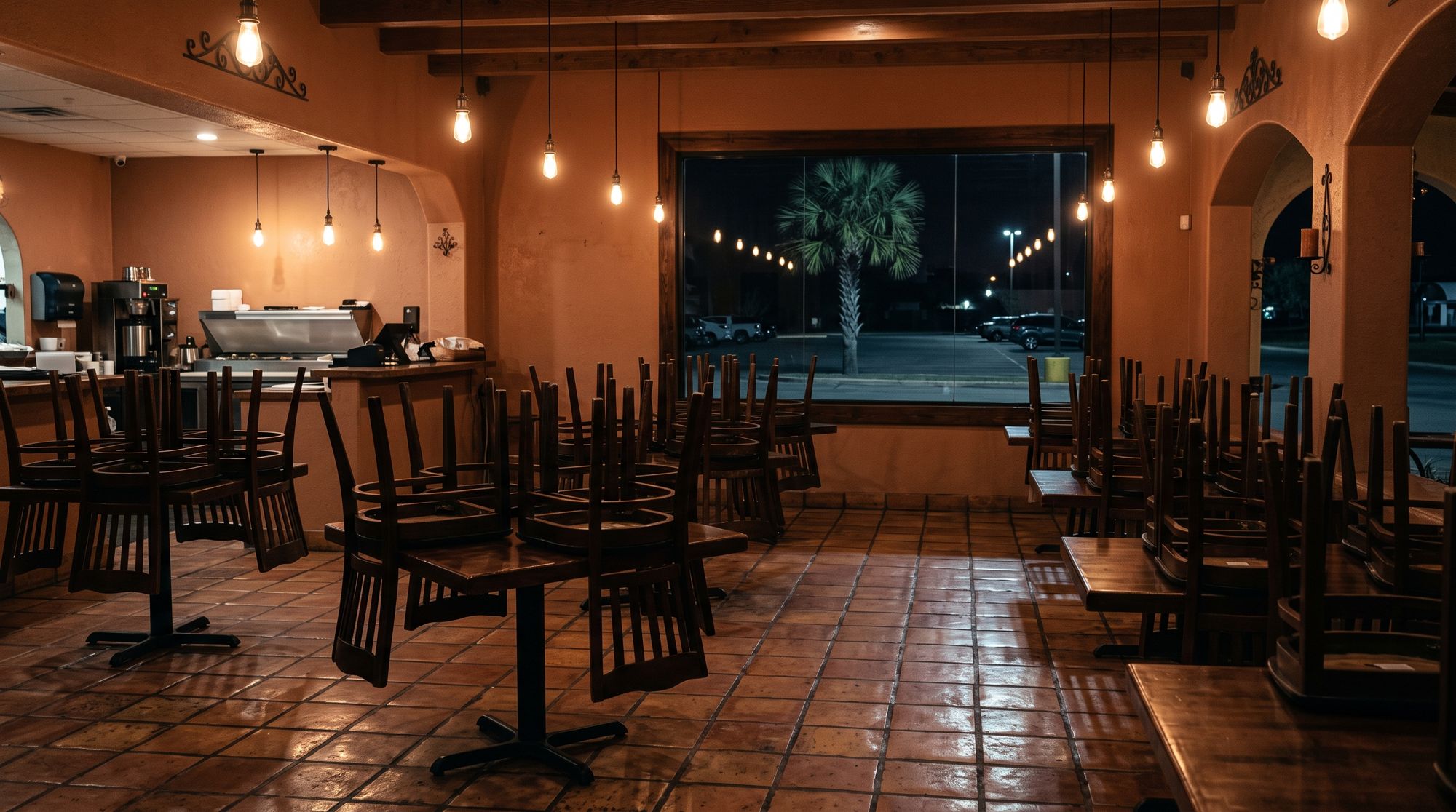 An empty restaurant dining room after closing, chairs up on the tables and lights low